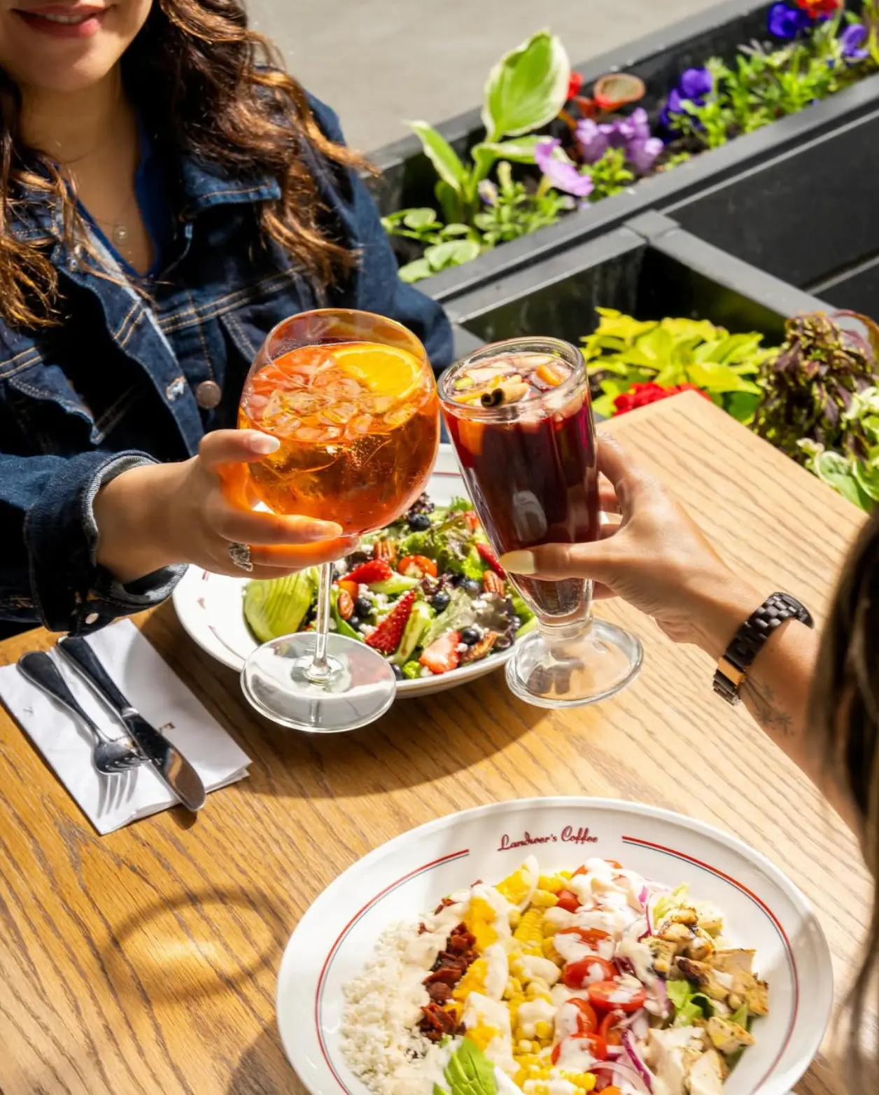 Two guests toasting spritz and sangria over a sunlit patio table at Cafe Landwer